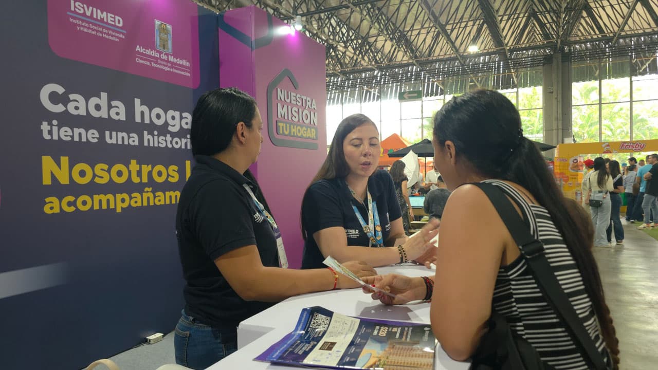 Personal de Isvimed orienta a una visitante en un stand de vivienda. Foto de contexto · fecha de toma no verificada.