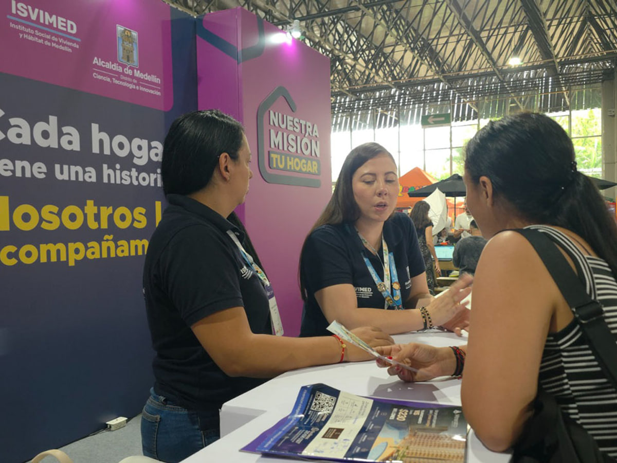 Personal de Isvimed orienta a una visitante en un stand de vivienda. Foto de contexto · fecha de toma no verificada.